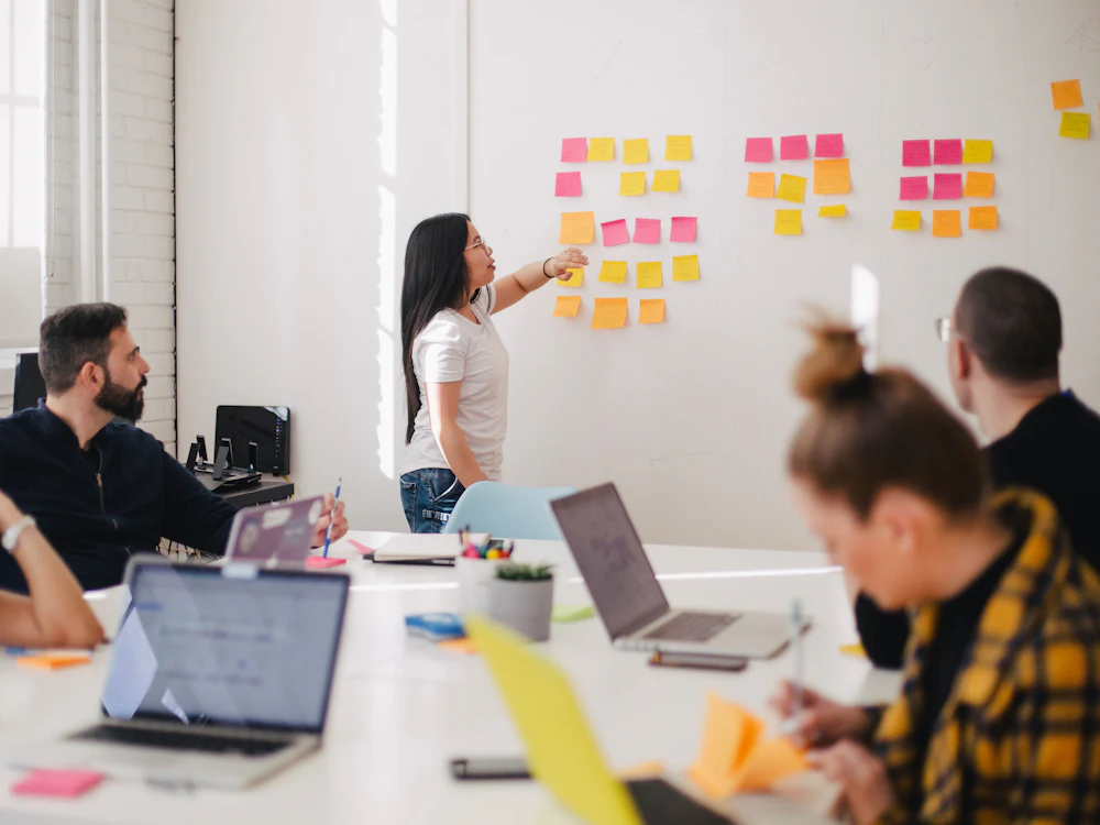 Team members in a planning workshop with sticky notes on a whiteboard and laptops on the table
